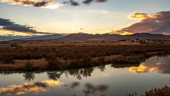 Time lapse of a cloudscape reflecting off a glassy river at sunset with mountains in the distance alt