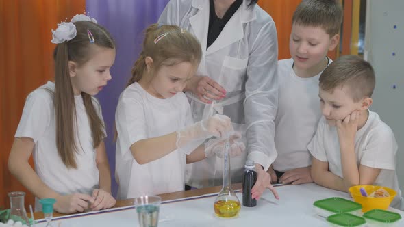 Chemical Experiments for Children. Girl Pours a Blue Liquid Into a Flask with a Yellow Liquid. Room alt