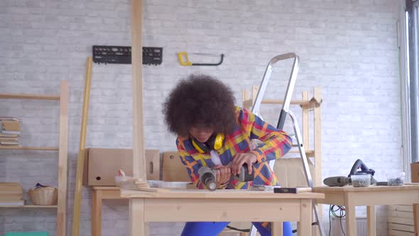 African Woman with an Afro Hairstyle Works on Wood in the Workshop alt