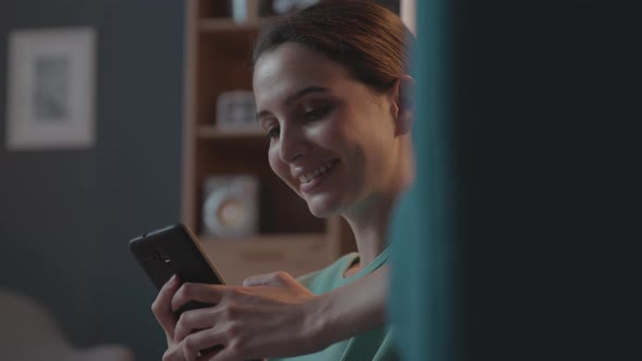 Happy woman relaxing at home and chatting with her phone