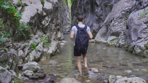Young man walking in running water in canyon, barefoot. alt