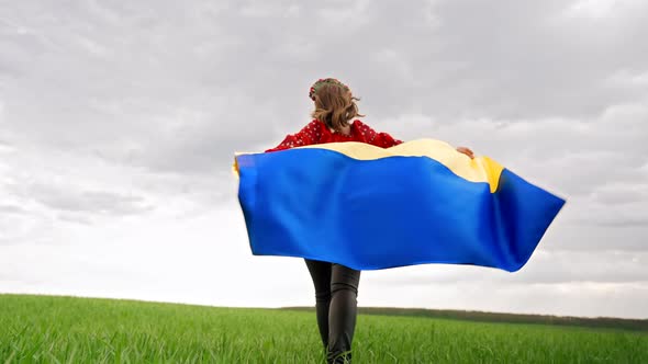 Happy Ukrainian Woman Running with National Flag Outdoors in Green Field alt