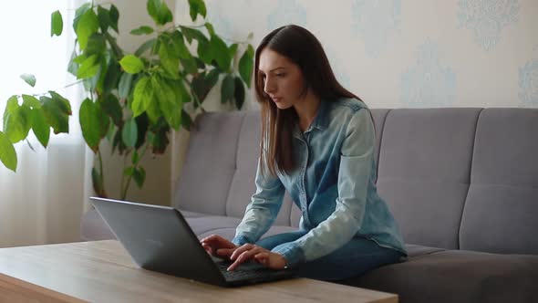 Angry Brunette Types on Laptop and Closes Sitting on Sofa alt