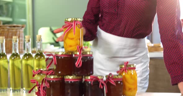 Female staff showing jars of preserves and olive oil on counter alt