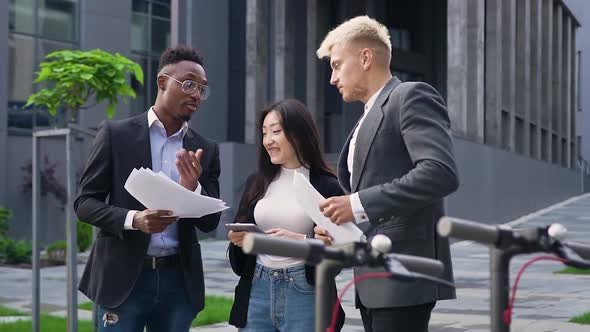 Stylish Multiethnic Youth Talking Near Modern Urban Building and Analyzing Financial Reports alt