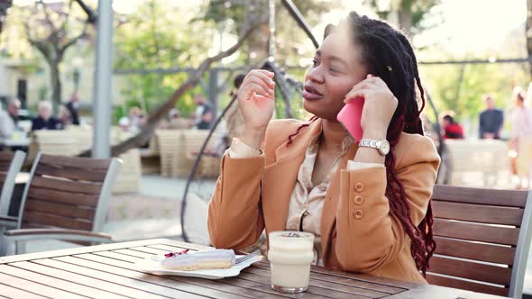 African American Woman Sitting in Outdoor Cafe and Talking on the Phone alt