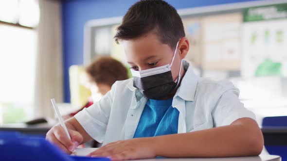 Portrait of mixed race schoolboy wearing face mask in classroom looking at camera alt