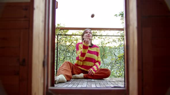 Woman Sits on Her Balcony in Sweater and Juggles Fruit in Her Spare Time alt