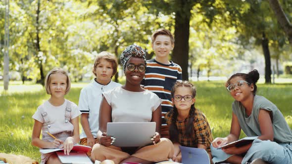 Happy Multiethnic Schoolchildren and Female Teacher Posing Together in Park alt