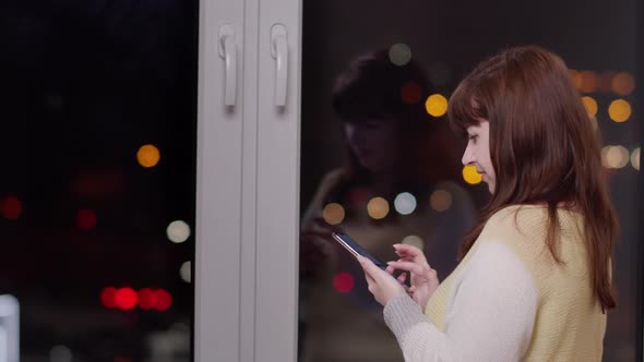 Woman Near the Window at Night and Uses the Phone Traffic Lights