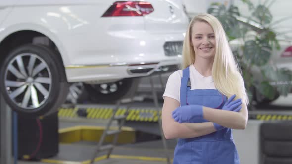 Middle Shot of Young Caucasian Woman Crossing Hands and Smiling. Blond Female Auto Mechanic Posing alt