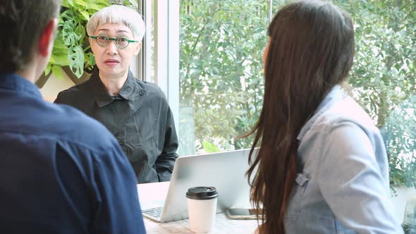 Senior woman talking about agreement of project and explaining with businesspeople in the cafe. alt