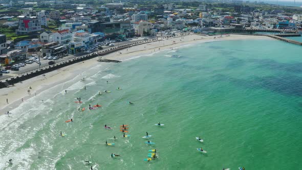 People surfing on a blue beach with a small harbor alt