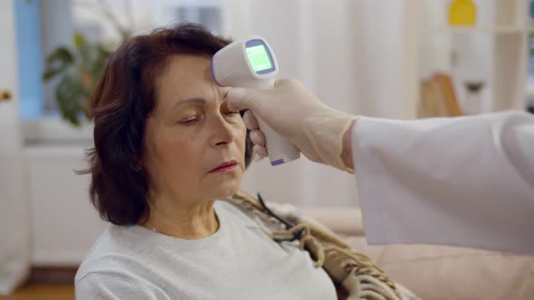 Doctor in Gloves Measures Patient Temperature with Noncontact Infrared Thermometer alt