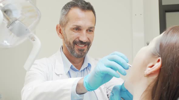 Experienced Male Dentist Smiling While Checking Teeth of a Patient