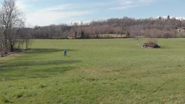Aerial: man having fun by riding mountain bike in the grass on sunny day, scenic alpine landscape, alt