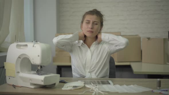 Camera Approaches To Tired Young Tailor with Tablet Stretching Neck and Sighing. Portrait of alt