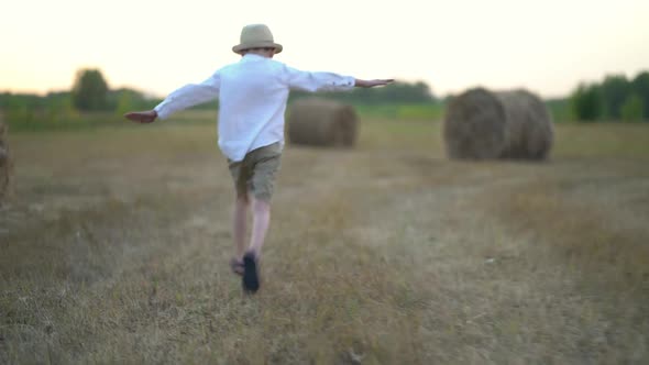 Boy Running in a Field with Haystacks