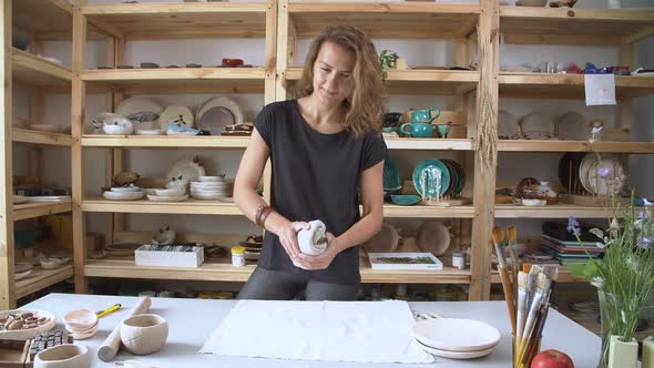 Young Woman Works in a Stylish Ceramic Studio. A Young Girl Holds a Ceramist Clay Lump in Her Hands