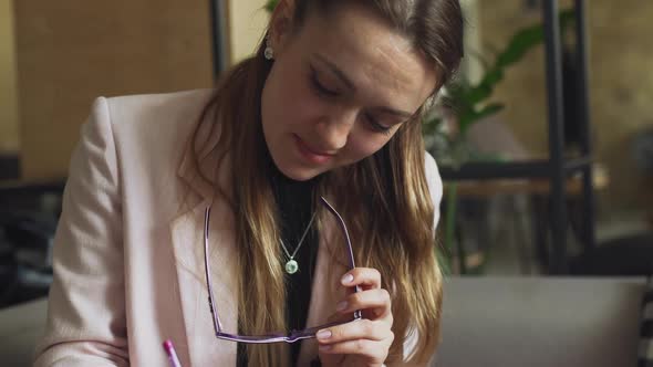 Theme Modern Profession for Young Women. Beautiful Girl with Glasses Sitting at Wooden Table Inside alt