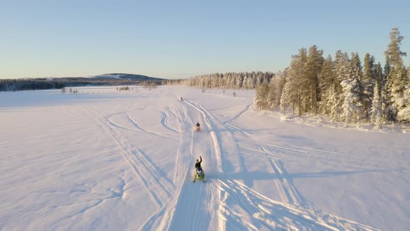 Aerial view above three snowmobiles riding across snowy Lapland Sweden wilderness trail alt