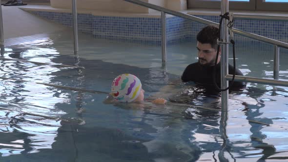 At the medical clinic Evexia in pool doctor watching for little boy who swims and holds railing alt