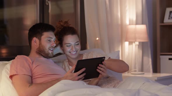 Happy Couple Using Tablet Computer in Bed at Night alt