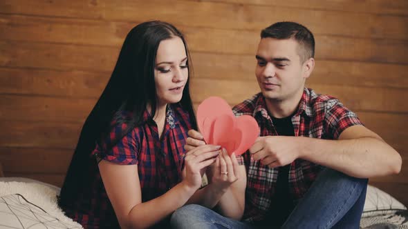 Beautiful couple are laying out in their hands red paper hearts of large and small sizes alt
