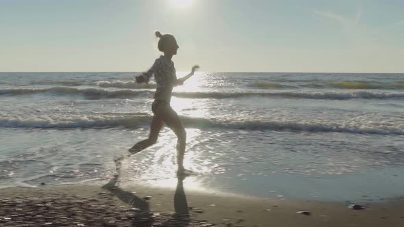 A slender woman runs and jumps on the waves of sea water on a sandy beach. alt