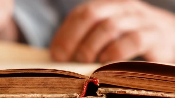 The concept of the study of old books.Close-up male hands in defocus flipping through the pages of a alt