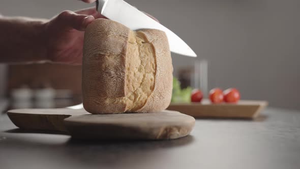 Man Slicing Small Ciabatta Bun for Sandwich on Kitchen Countertop alt