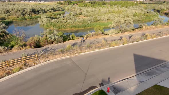 Man riding a bicycle along a path next to a river with the sky reflecting off the surface of the wat alt
