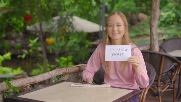 In a Cafe, a Young Woman Refuses To Take a Single-use Plastic Drinking Straw. She Is Holding a Paper alt
