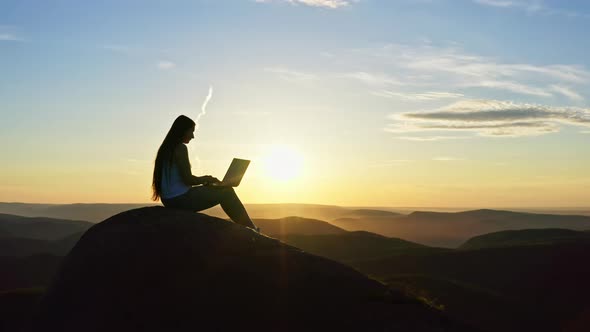Drone Shot of a Female Freelancer with a Laptop on a Mountaintop at Sunset