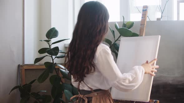 Young Woman Artist Puts a Canvas on Easel  Takes the Palette and Brush to Start Painting alt