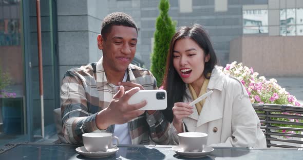 Attractive Loving Couple in Outdoor Cafe Hugging Each Other and Talking By Video Call on Mobile alt