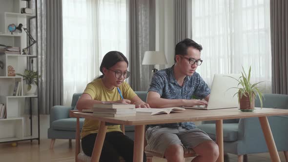 Asian Father Working With Laptop And Daughter Doing Homework At Living Room alt