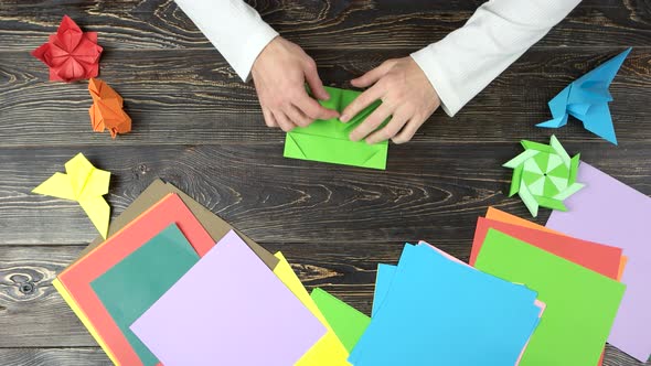 Man Folding Origami From Green Paper. alt