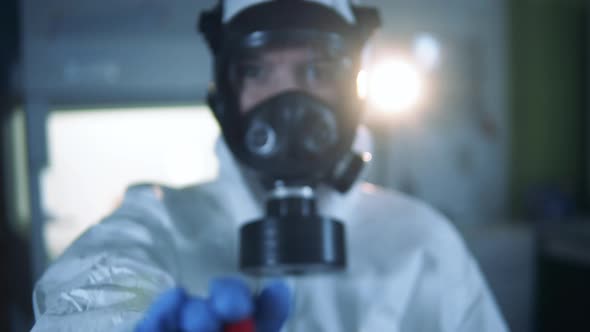 Specialist in a Hazmat Suit is Showing a Coronavirus Test Tube alt