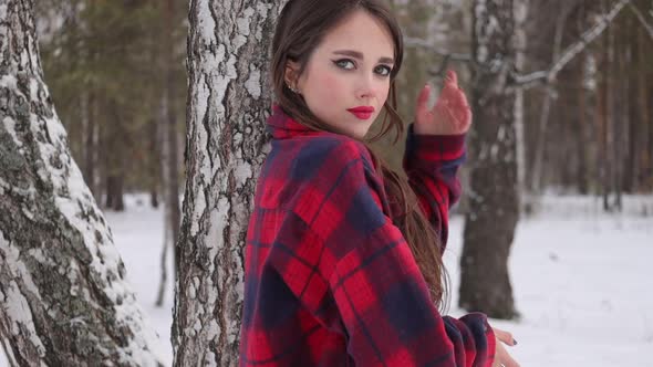 Young Woman with Wavy Hair Standing and Touching Face in Winter Forest