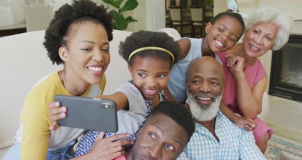 Happy african american family sitting and using smartphone in living room alt