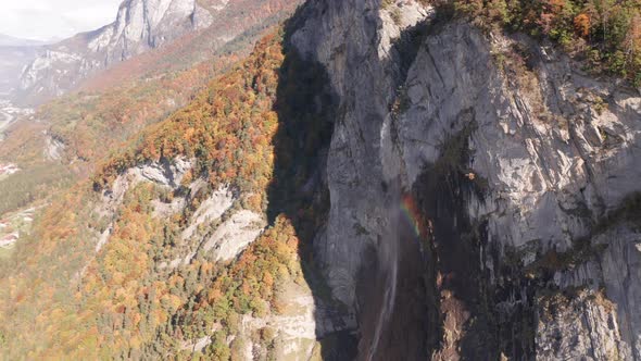 Aerial of beautiful small waterfall spawning a rainbow with a colorful forest in autumn in the backg alt