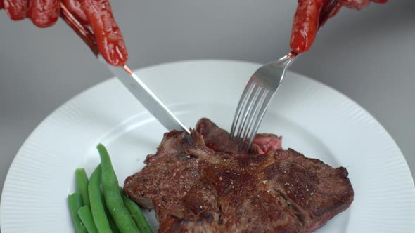 Bloody Male Hands Man Eats Beef Steak Cutting Off Piece of Meat on White Plate with Knife and Fork alt