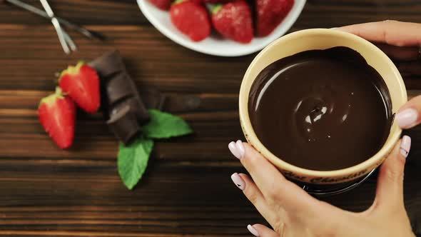 The Chef's Hands Put the Fondue on the Table. Fondue with Chocolate Strawberries on a Wooden alt