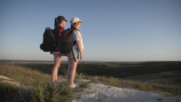 Mother and Daughter on Top of a Mountain. Hikers with Backpack Standing on Cliff and Looking To a alt