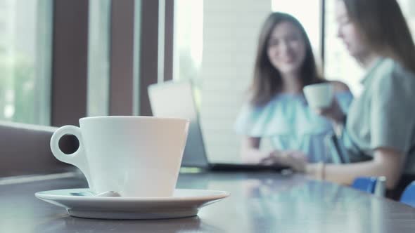 Cup of Coffee on the Table of Two Students Working on a Project on Background alt