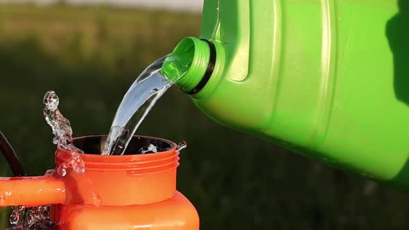 In summer, the gardener pours gasoline from a plastic canister to another in the yard.