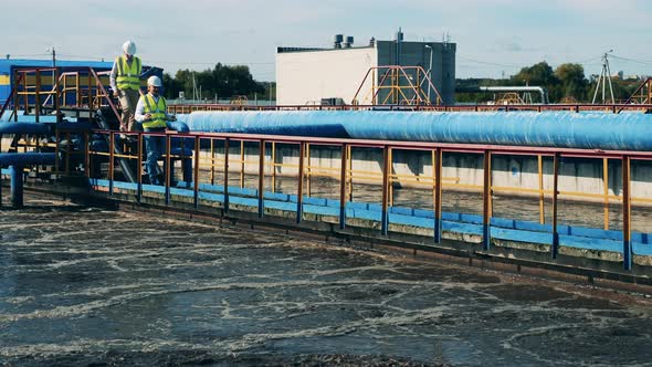 Two Wastewater Operators Walking Along Pipes at a Water Cleaning Plant alt
