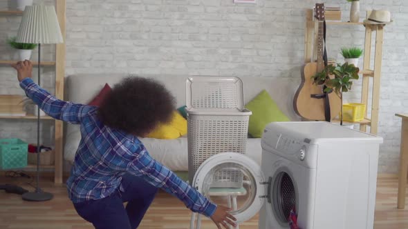 Close Up Happy African Woman with an Afro Hairstyle Throws Dirty Clothes in the Washing Machine Like alt