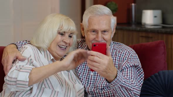 Grandmother and Grandfather Making Video Call Online on Mobile Phone at Home. Smiling Elderly Couple alt
